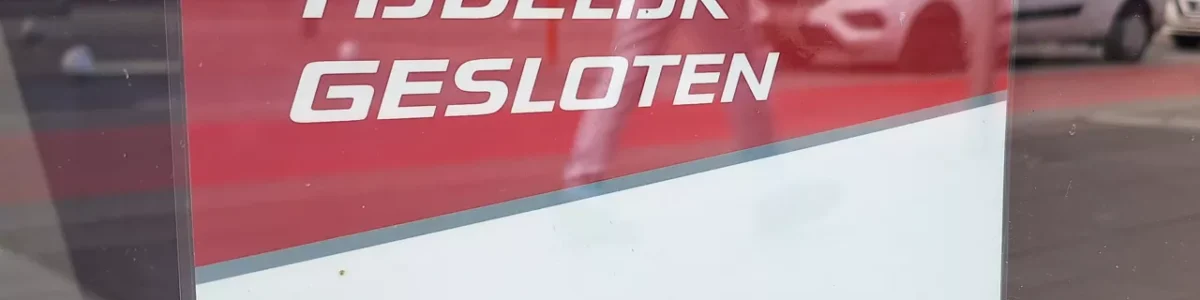 Red and white sign in a window with the text "temporarily closed" in dutch.