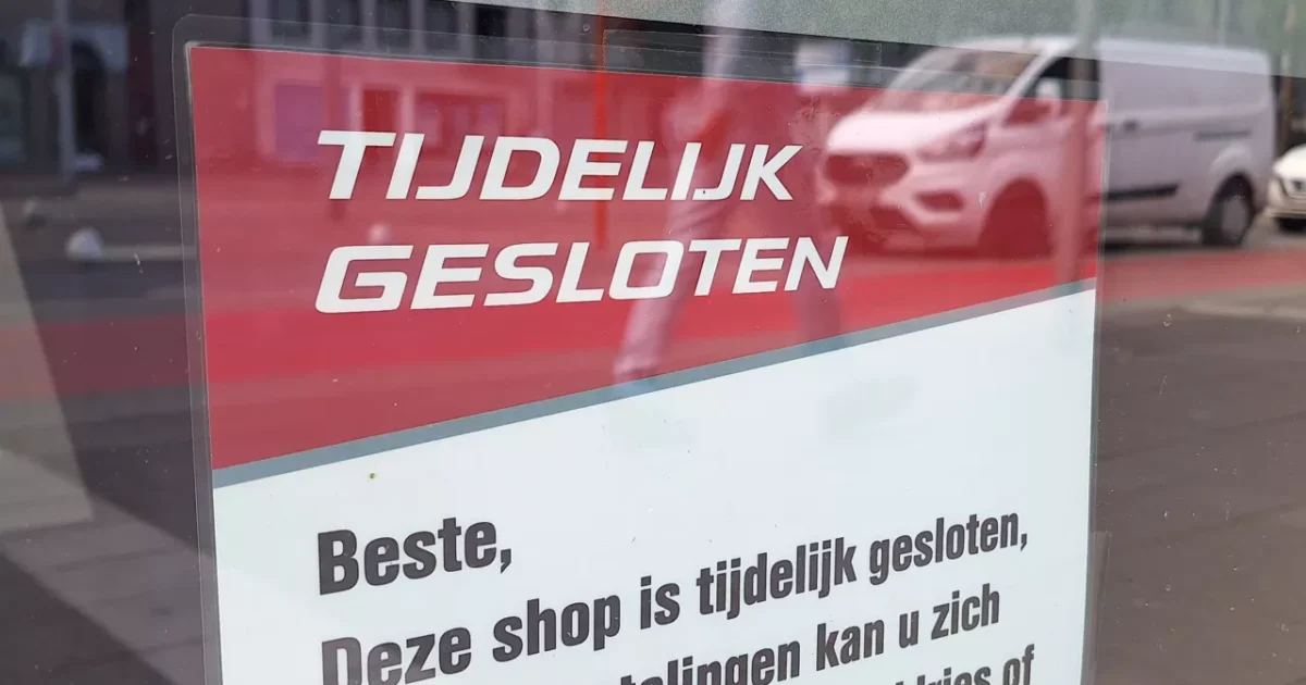 Panneau rouge et blanc dans une fenêtre avec le texte « temporairement fermé » en néerlandais.