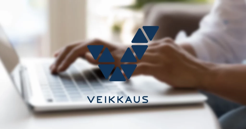 Veikkaus logo on a blurred background showing a person typing on a laptop keyboard