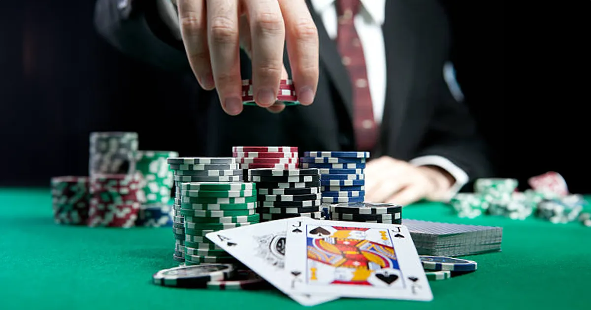 Een hand gevuld met fiches met op de voorgrond een schoppenboer en een schoppenaas die een blackjack.
