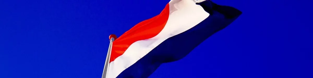 The dutch flag against a royal blue sky background.