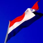 The dutch flag against a royal blue sky background.