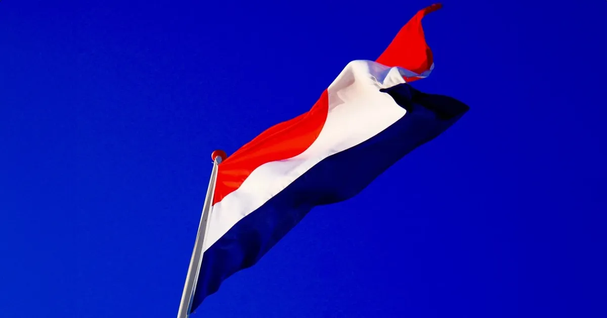 The dutch flag against a royal blue sky background.