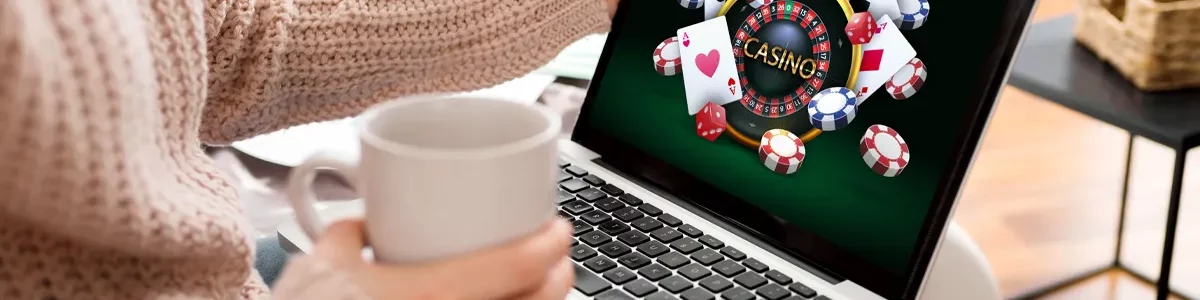 Online casino-afbeelding op een laptop die wordt vastgehouden door een vrouw die uit een kopje drinkt.
