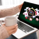 Online casino image on a laptop held by a woman drinking from a cup.