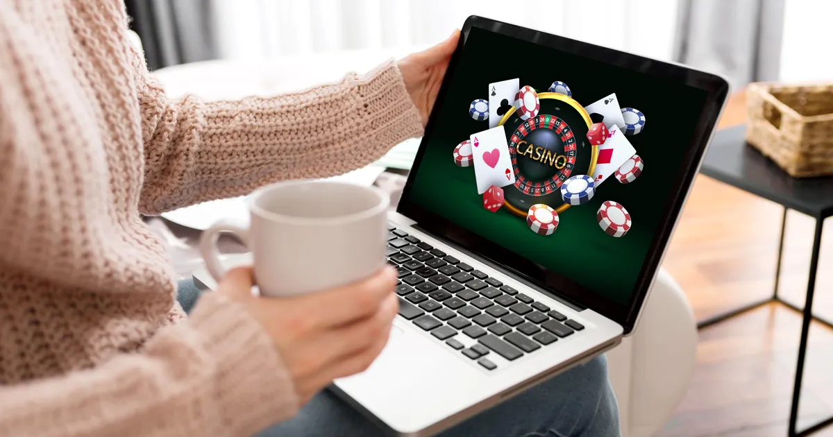 Image casino en ligne sur un laptop tenu par une femme buvant dans une tasse.